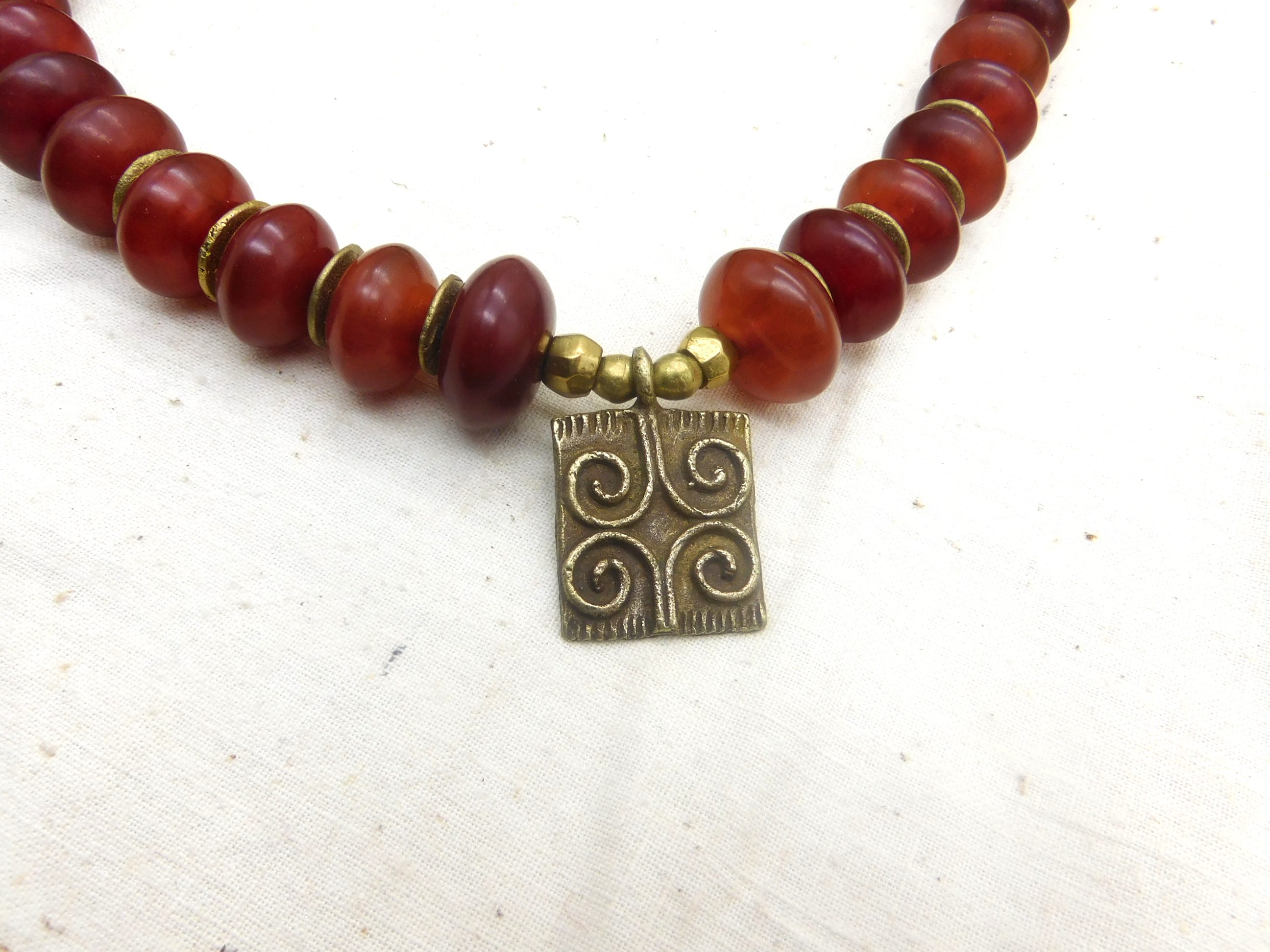 African inspired necklace with resin amber beads and a handmade brass pendant with a Sankofa symbol